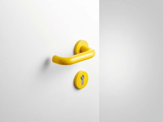 Yellow synthetic material door handle and matching rose with keyhole in front of a white painted door