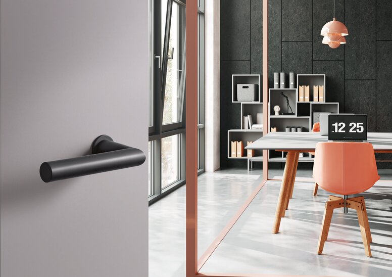 HEWI System 162 lever handle A black synthetic material door handle on a grey door; behind it, an office with a desk and chair in front of a dark grey wall