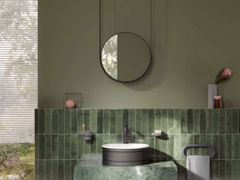 A round washbasin set on a green marble vanity unit with a black tap and towel holder, with a round mirror above it