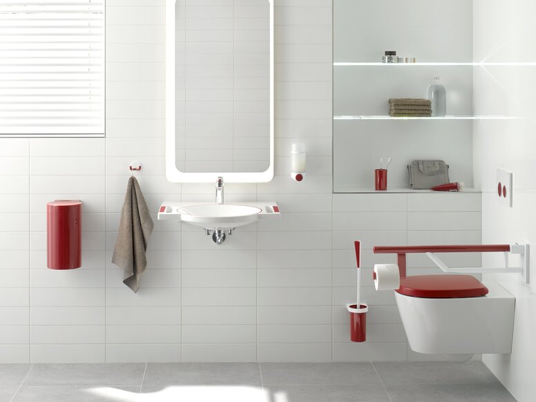 HEWI System 800K Interior A red hinged support rail next to the WC with a red cover, alongside a white washbasin with red recessed handles, and an illuminated mirror above it