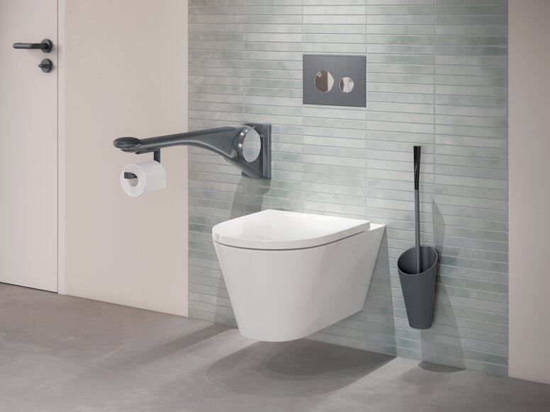 HEWI Serie 802 LifeSystem Stützklappgriff Premium Wandhängendes WC mit seitlichem Haltegriff, integriertem WC-Papierhalter sowie einer an grüner Fliesenwand montierten Toilettenbürste