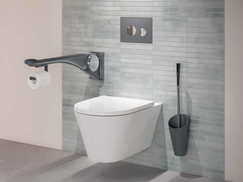 HEWI Serie 802 LifeSystem Stützklappgriff Premium Wandhängendes WC mit seitlichem Haltegriff, integriertem WC-Papierhalter sowie einer an grüner Fliesenwand montierten Toilettenbürste