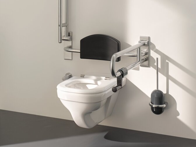 WC with a hinged backrest and two hinged support handles fitted on the left and right in the area of accessibility against a white wall