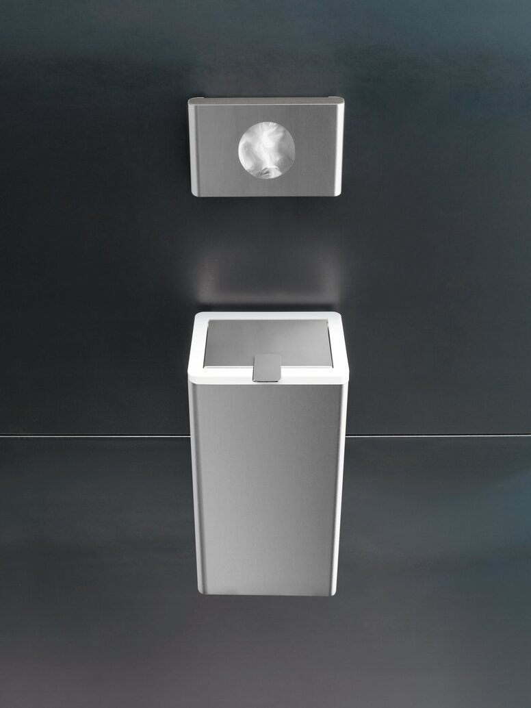 HEWI Range 805 hygiene bag dispenser Rectangular stainless steel hygiene bag dispenser mounted above a matching waste bin on a dark grey wall