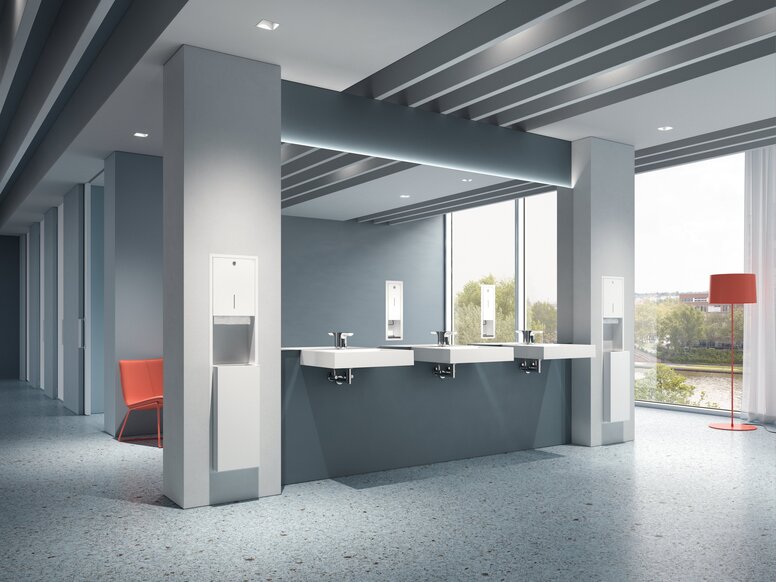 Three white wall-mounted washbasins with single-lever taps and three white soap dispensers mounted on columns in the public WC