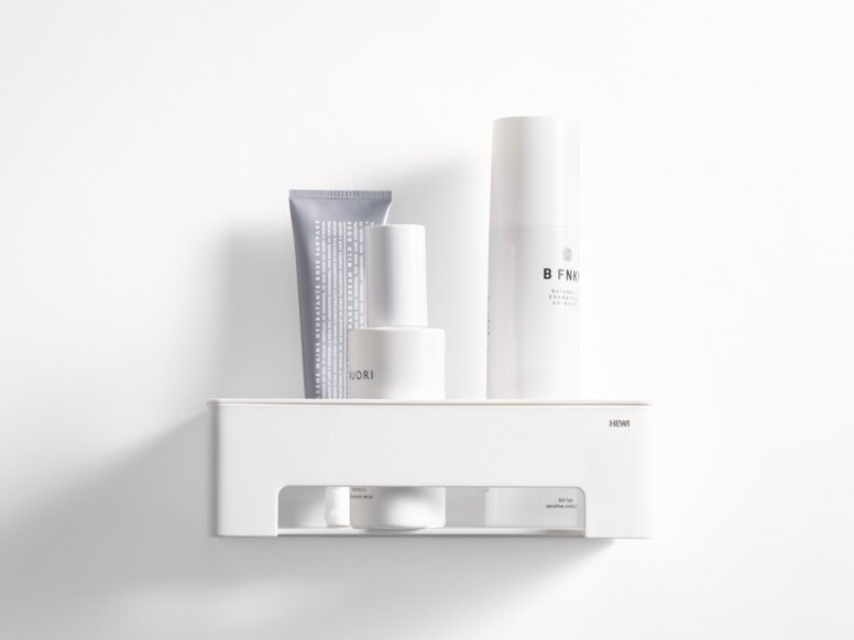 White wall-mounted shower basket with a shelf and an open compartment containing toiletries on a white wall