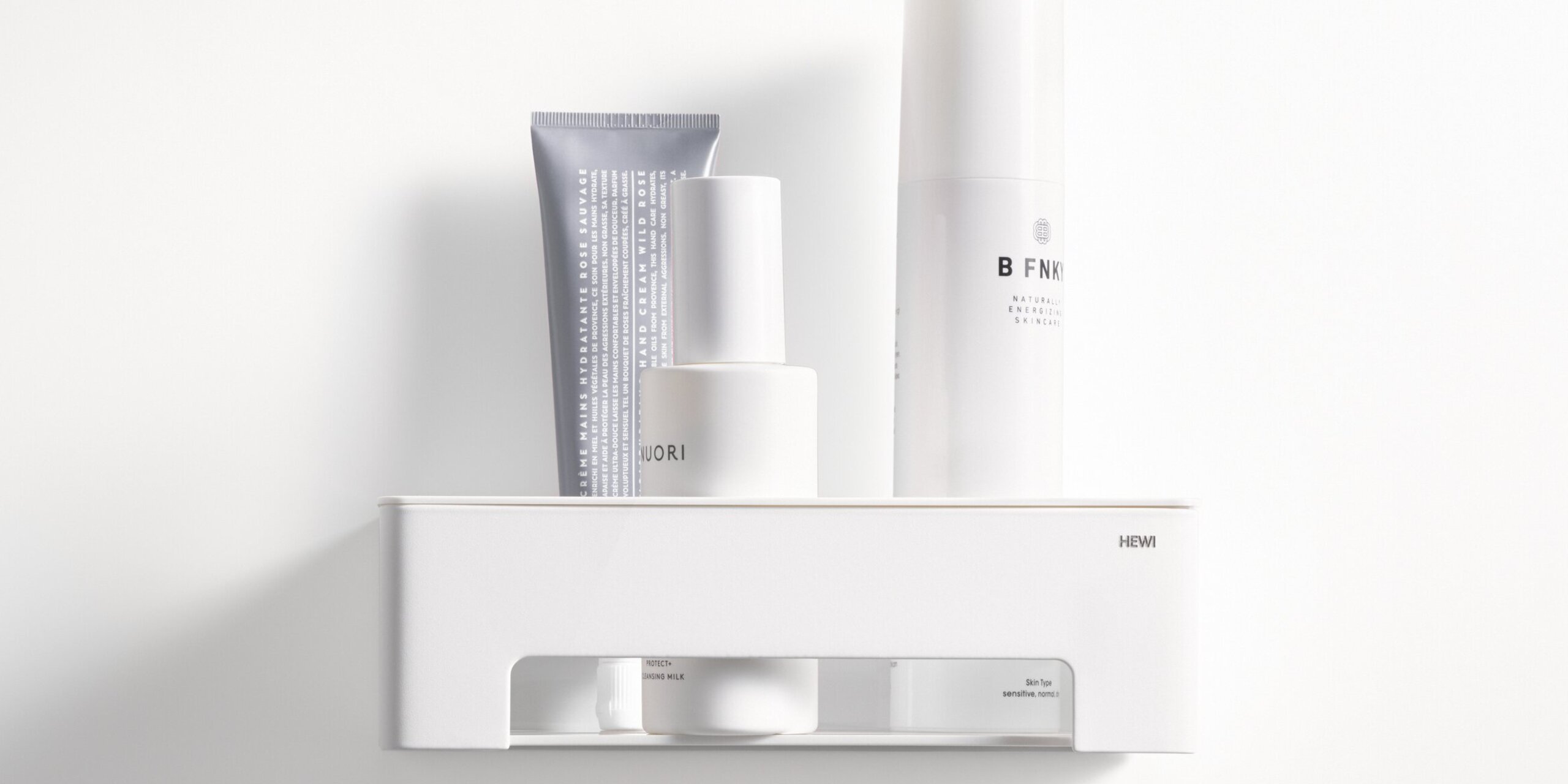 White wall-mounted shower basket with a shelf and an open compartment containing toiletries on a white wall