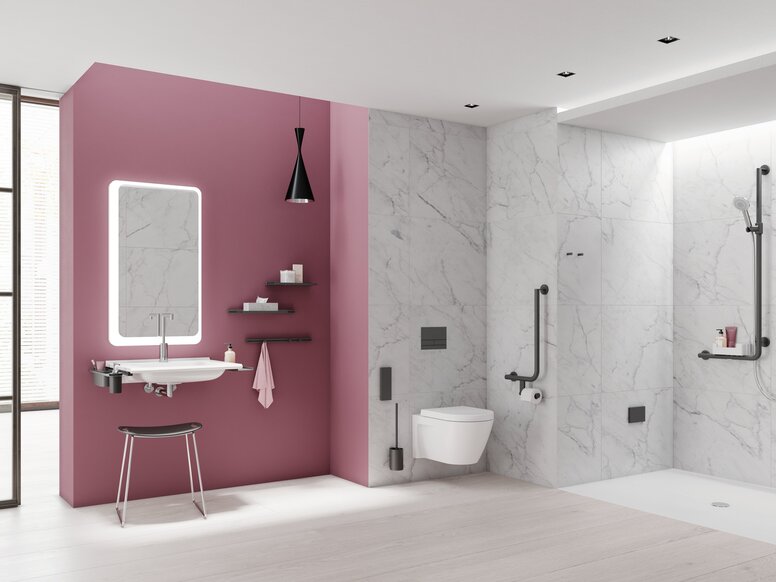 HEWI System 900 Bathroom Interior Modern bathroom with a pink wall behind the washbasin, illuminated mirror, wall-hung toilet and level-access shower with white and grey marble-effect tiles, complemented by black grab rails and fittings